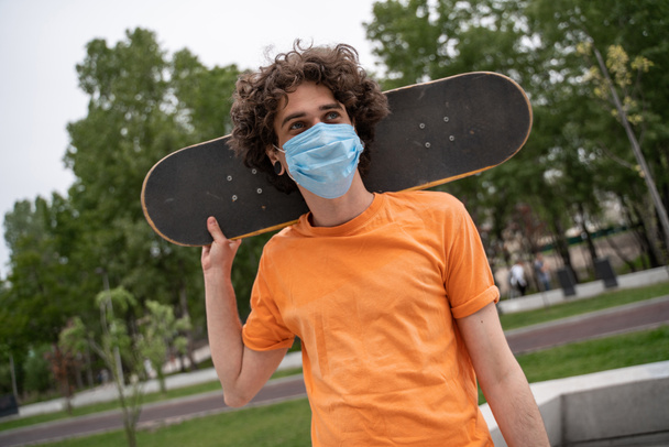 Junger Mann mit Schutzmaske schaut weg, während er Schlittschuh hinter dem Hals hält - Foto, Bild