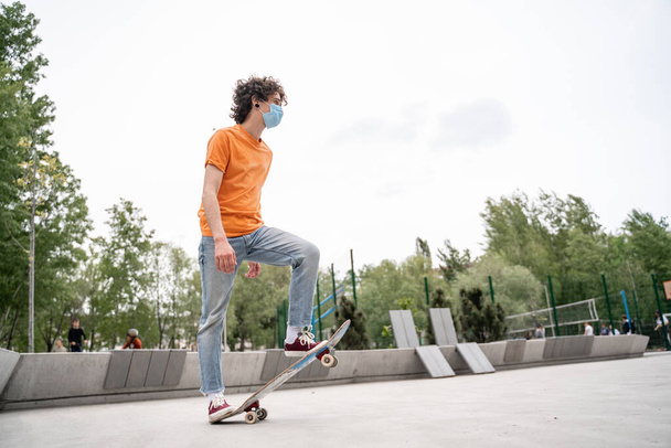 молодой человек в медицинской маске катается на скейтборде в скейт-парке - Фото, изображение