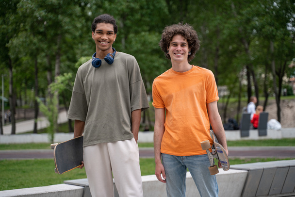 vrolijke interraciale vrienden met skateboards glimlachen op camera buiten - Foto, afbeelding
