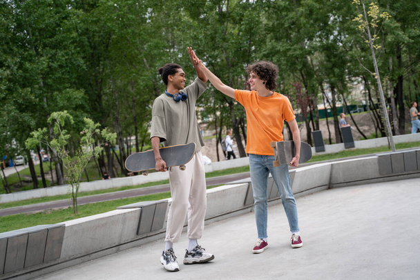 full length view of multiethnic skateboarders giving high five in skate park - Foto, afbeelding