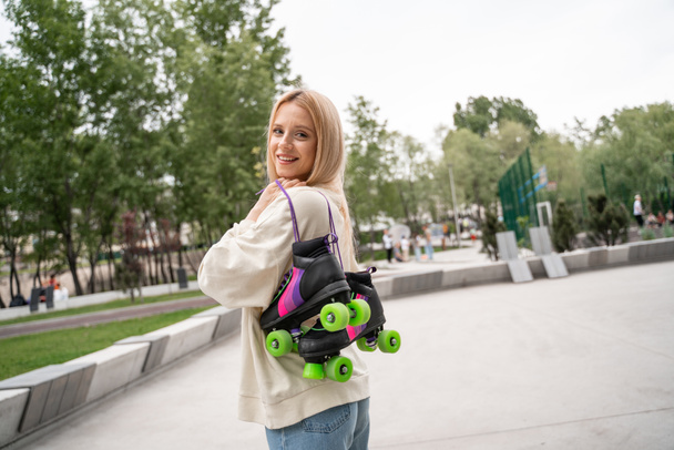jong blond vrouw met rolschaatsen kijken naar camera in skate park - Foto, afbeelding
