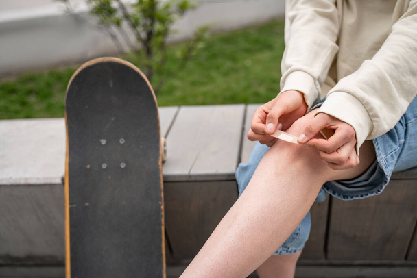 cropped view of skateboarder applying adhesive plaster on injured knee - Valokuva, kuva