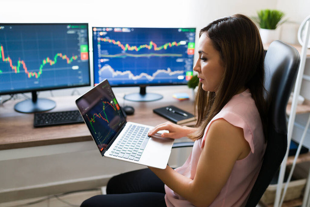 Zakenvrouw koopt aandelen online. Spaanse jonge vrouw werken vanuit huis op haar handel bedrijf op een laptop - Foto, afbeelding