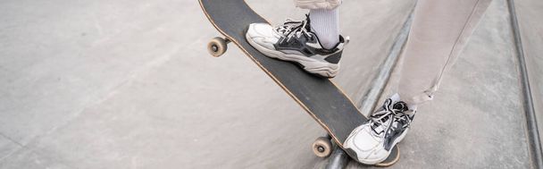 vista parcial del hombre en zapatillas deportivas monopatín en rampa de skate, bandera - Foto, Imagen