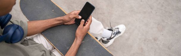 アフリカ系アメリカ人のスケーターの一部が屋外のブランクスクリーンのスマートフォンで - 写真・画像