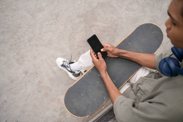 vysoký úhel pohledu oříznutý africký americký bruslař pomocí mobilního telefonu s prázdnou obrazovkou - Fotografie, Obrázek