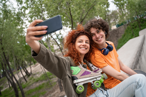 Glückliche Frau mit Rollschuhen macht Selfie mit lockigem Freund im Park - Foto, Bild