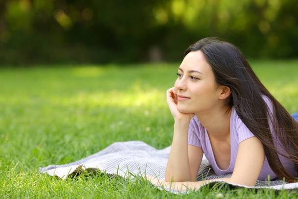 Mixed race woman contemplating and thinking lying on the grass in a park - Photo, Image
