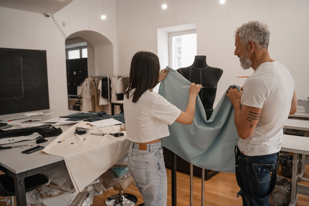 Мультиэтнические дизайнеры держат ткань возле манекена в мастерской  - Фото, изображение