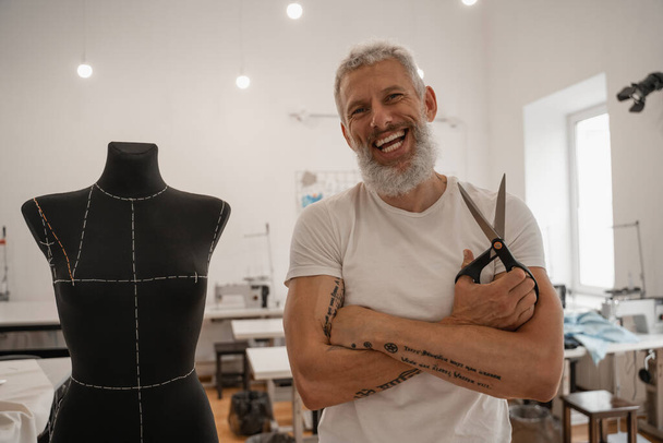 Cheerful designer with scissors looking at camera near mannequin  - Photo, Image
