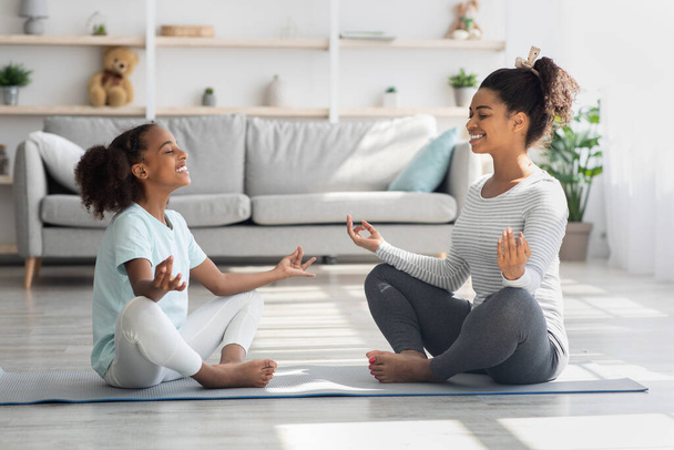Sportowa czarna rodzina matka i córka medytują w domu - Zdjęcie, obraz
