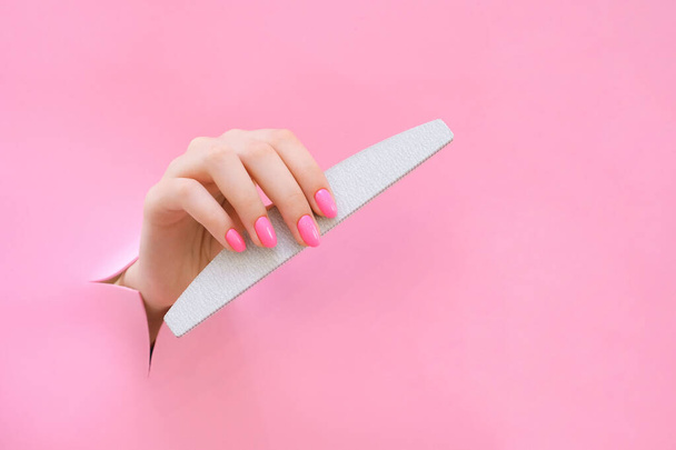nail file in the hand of a young woman on a pink background from the hole. copy space - Φωτογραφία, εικόνα