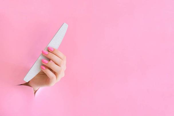 nail file in the hand of a young woman on a pink background from the hole. copy space - Foto, immagini