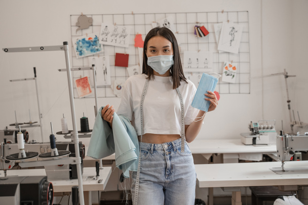 Азиатский дизайнер в медицинской маске держит ткань в ателье  - Фото, изображение