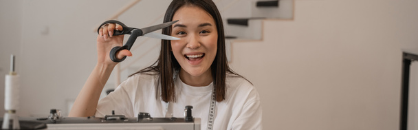 sonriente asiático diseñador holding costura tijeras en estudio, banner  - Foto, Imagen