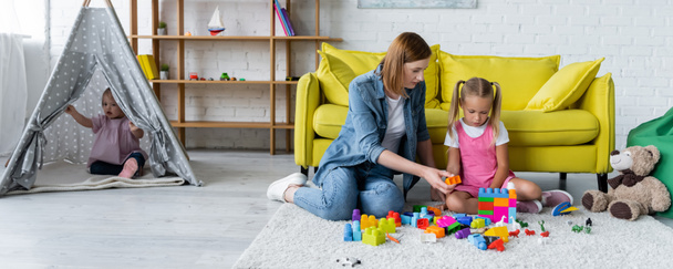 kindergarten teacher playing building blocks with preschooler girl while kid with down syndrome sitting in tipi, banner - Photo, Image