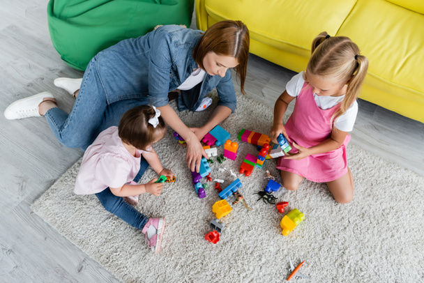 high angle view of kindergarten teacher playing building blocks with preschooler girl and toddler kid with down syndrome  - Фото, зображення