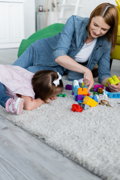toddler girl with down syndrome playing with happy kindergarten teacher on carpet  - Fotoğraf, Görsel