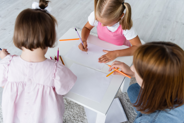 высокий угол зрения детей рисования на бумагах рядом с воспитателем детского сада  - Фото, изображение