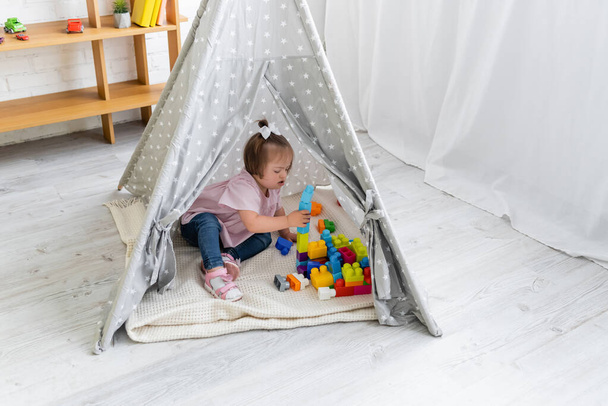 toddler girl with down syndrome playing building blocks in teepee tent  - 写真・画像