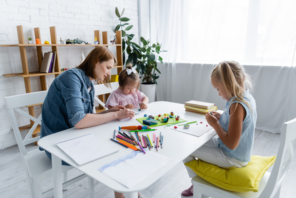 maestro de jardín de infantes moldeando plastilina con niño discapacitado y niña preescolar en la sala de juegos  - Foto, Imagen