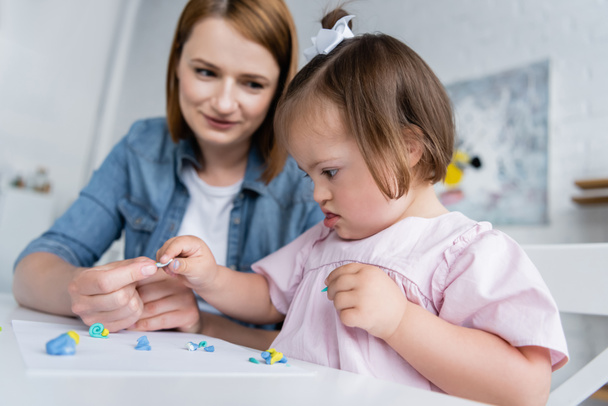 blurred kindergarten teacher molding plasticine with disabled kid with down syndrome  - Foto, imagen
