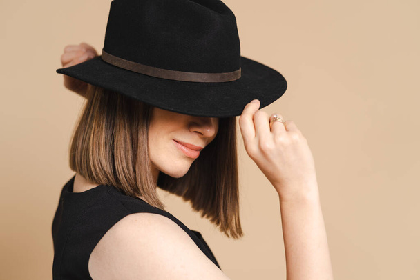 Frau mit schwarzem Hut und Kleid, Porträt auf beigem Hintergrund - Foto, Bild