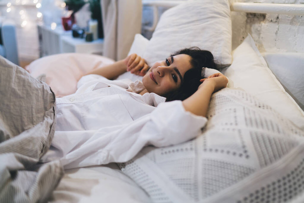 Беззаботная женщина чувствует мирное удовольствие в течение воскресного утра и долго лежал в постели, счастливая кавказская женщина расслабляясь в ленивый выходной день мечтая после пробуждения в удобной домашней спальне - Фото, изображение