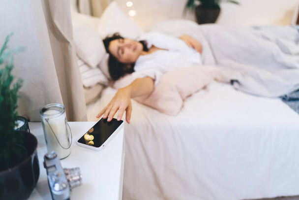 Blurred female turn off alarm signal on modern smartphone technology want sleep more during sunday morning, woman touching blank screen of digital cellphone gadget while awaking in home apartment - Zdjęcie, obraz