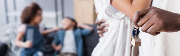 african american man holding key while hugging wife near blurred kids in new apartment, banner - Foto, Imagem
