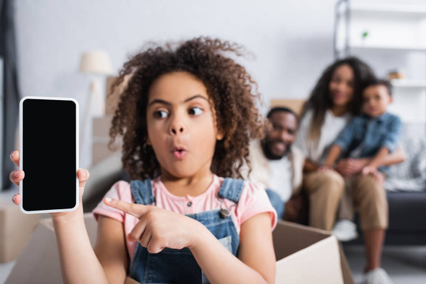 ámulatba ejtett afro-amerikai gyerek mutat okostelefon üres képernyőn, miközben ül a kartondobozban - Fotó, kép