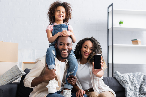 african american woman showing smartphone with blank screen near happy husband and daughter - Photo, Image