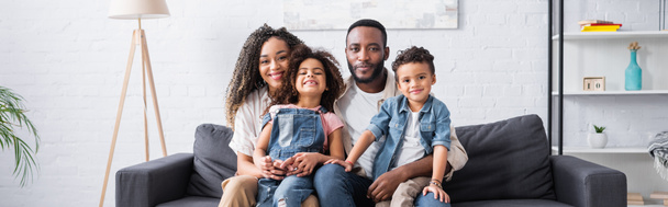 alegre afroamericano familia sonriendo a cámara en sofá en casa, pancarta - Foto, Imagen