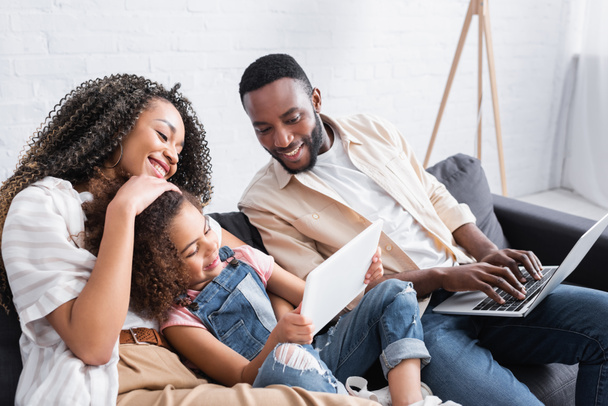 africano americano niño usando portátil cerca feliz madre y padre con portátil - Foto, Imagen