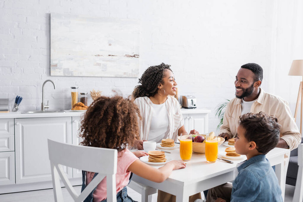 african american couple smiling during breakfast with children in kitchen - Fotó, kép