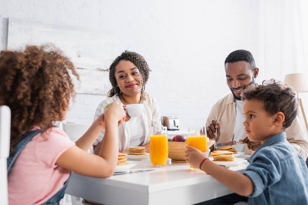african american woman with cup of coffee smiling during breakfast with family - Photo, Image