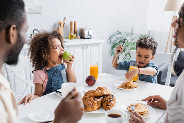 african american kid eating apple during breakfast with family - Фото, изображение