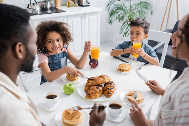 african american girl smiling near family and croissants during breakfast - Foto, afbeelding