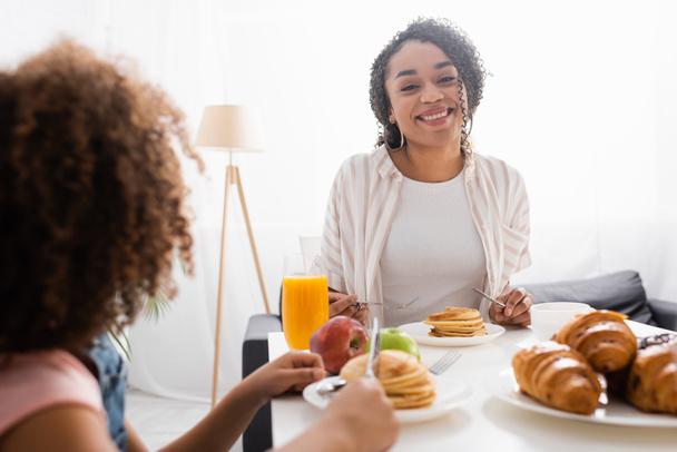 happy african american woman smiling near blurred daughter during breakfast - Foto, Imagen