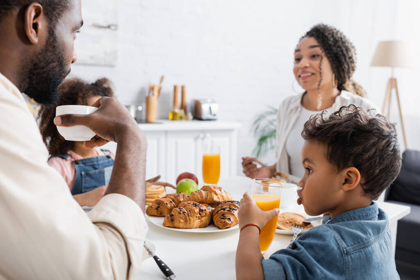 african american boy drinking orange juice during breakfast with family - Foto, afbeelding