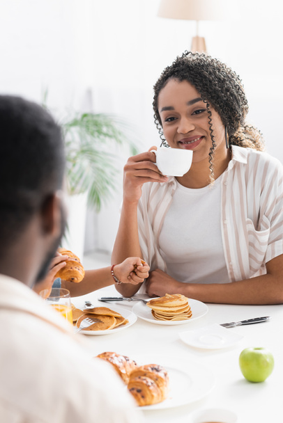 happy african american woman drinking coffee near son and blurred husband - Photo, Image