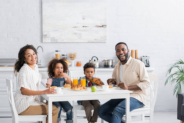 happy african american couple smiling at camera during breakfast in kitchen - Fotó, kép