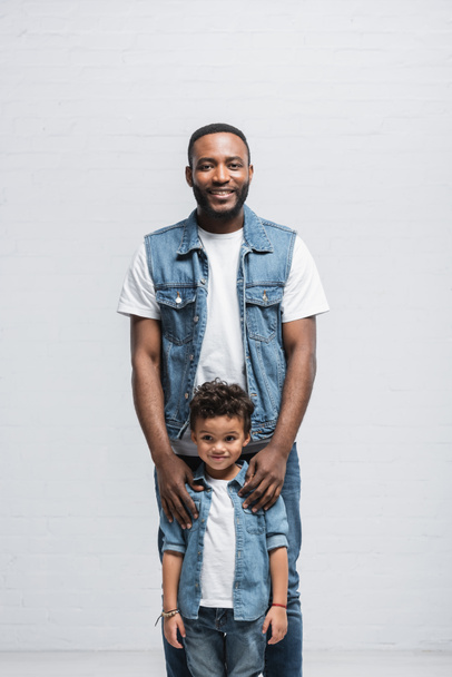 feliz afroamericano padre e hijo mirando la cámara en gris - Foto, Imagen