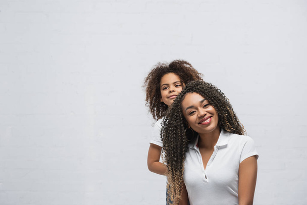 pleased african american woman smiling at camera near daughter on grey - Photo, image