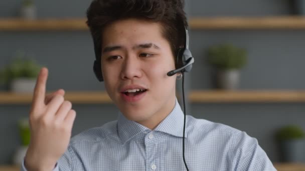 Портрет молодого уверенного азиата в наушниках, разговаривающего с камерой, объясняющего основы онлайн-бизнеса - Кадры, видео