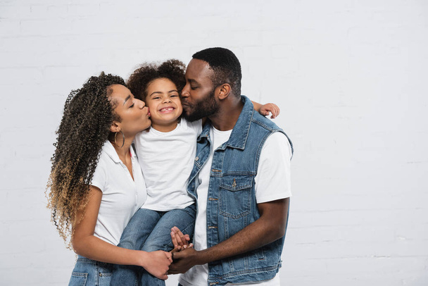 happy african american parents kissing smiling daughter on grey - Photo, Image