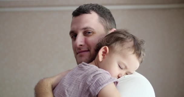 malé dítě usnulo v otcově náručí. táta houpe miminko, aby mohlo spát doma. close-up - Záběry, video