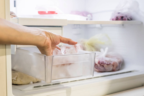 The girl takes out several pieces of ice from the compartment into the freezer. - Photo, Image