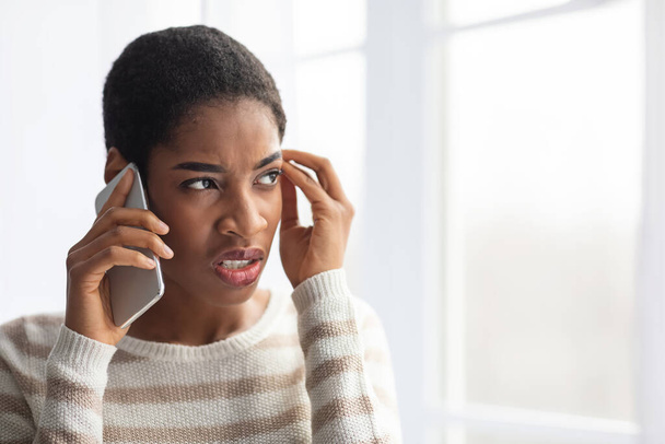 Afroamerikanerin leidet unter schlechter Verbindung, während sie zu Hause mit dem Handy spricht - Foto, Bild