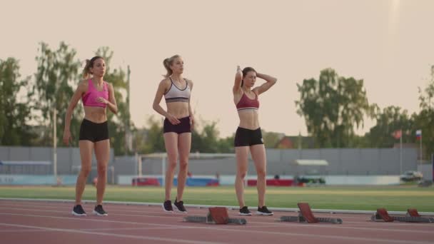 Drie vrouwelijke atleten gaan tegelijkertijd marathon lopen, rivaliteit, slow-motion. vrouwen die voor de race op een startlijn staan - Video